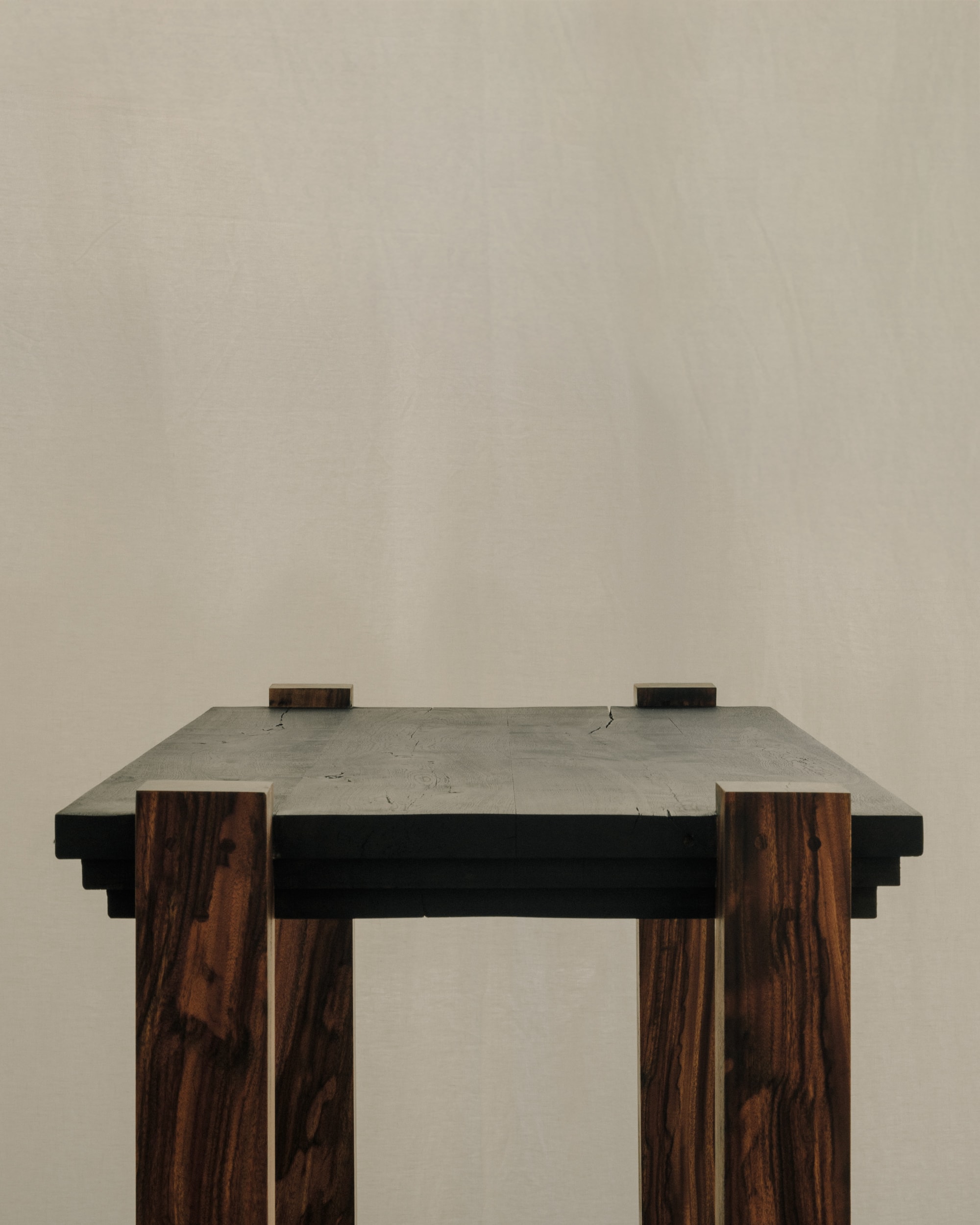Front view of a dark console desk with four mahogany legs against a plaster wall